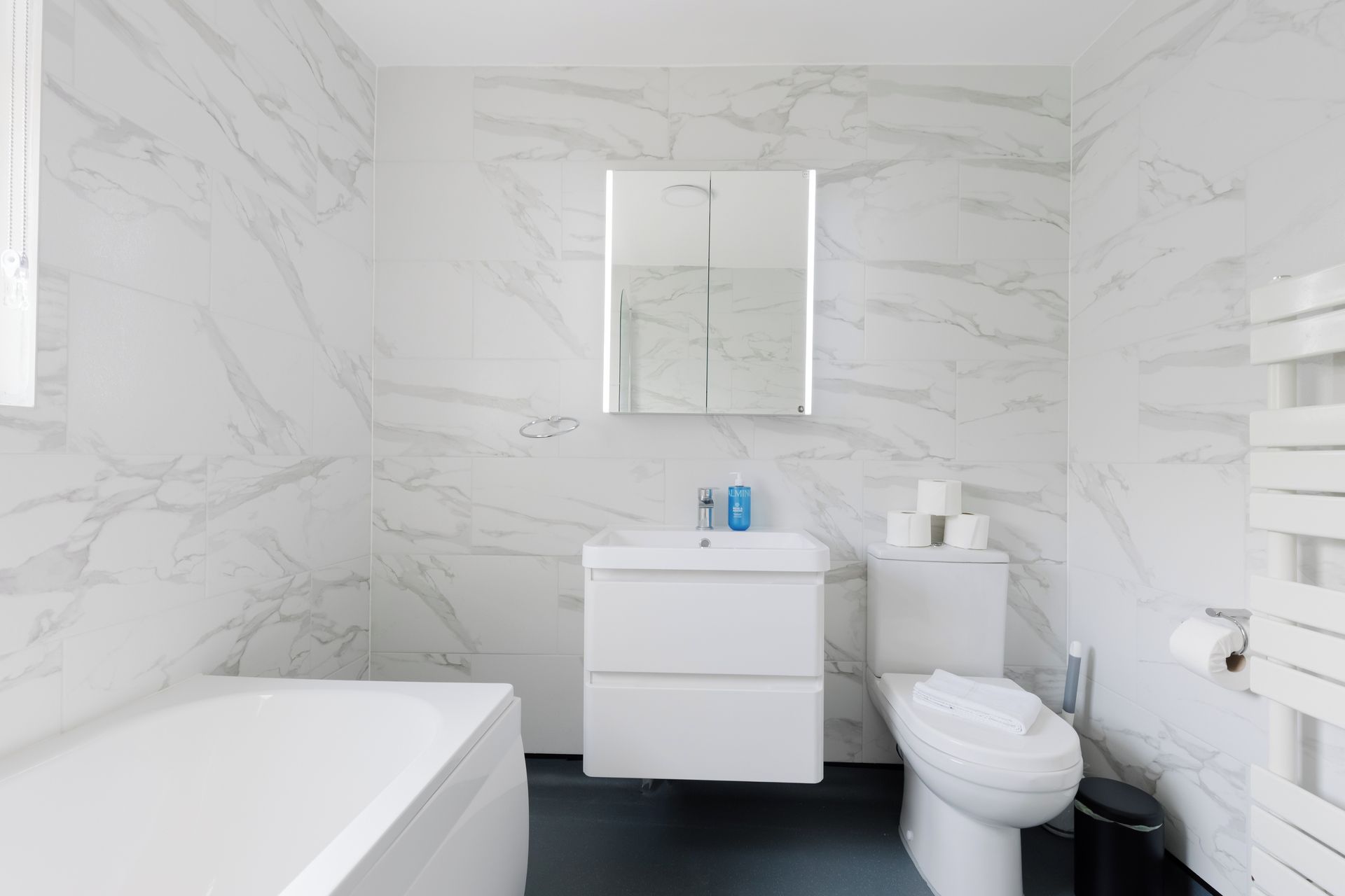 A bathroom with a marble wall, a white sink, a toilet, and a bathtub.