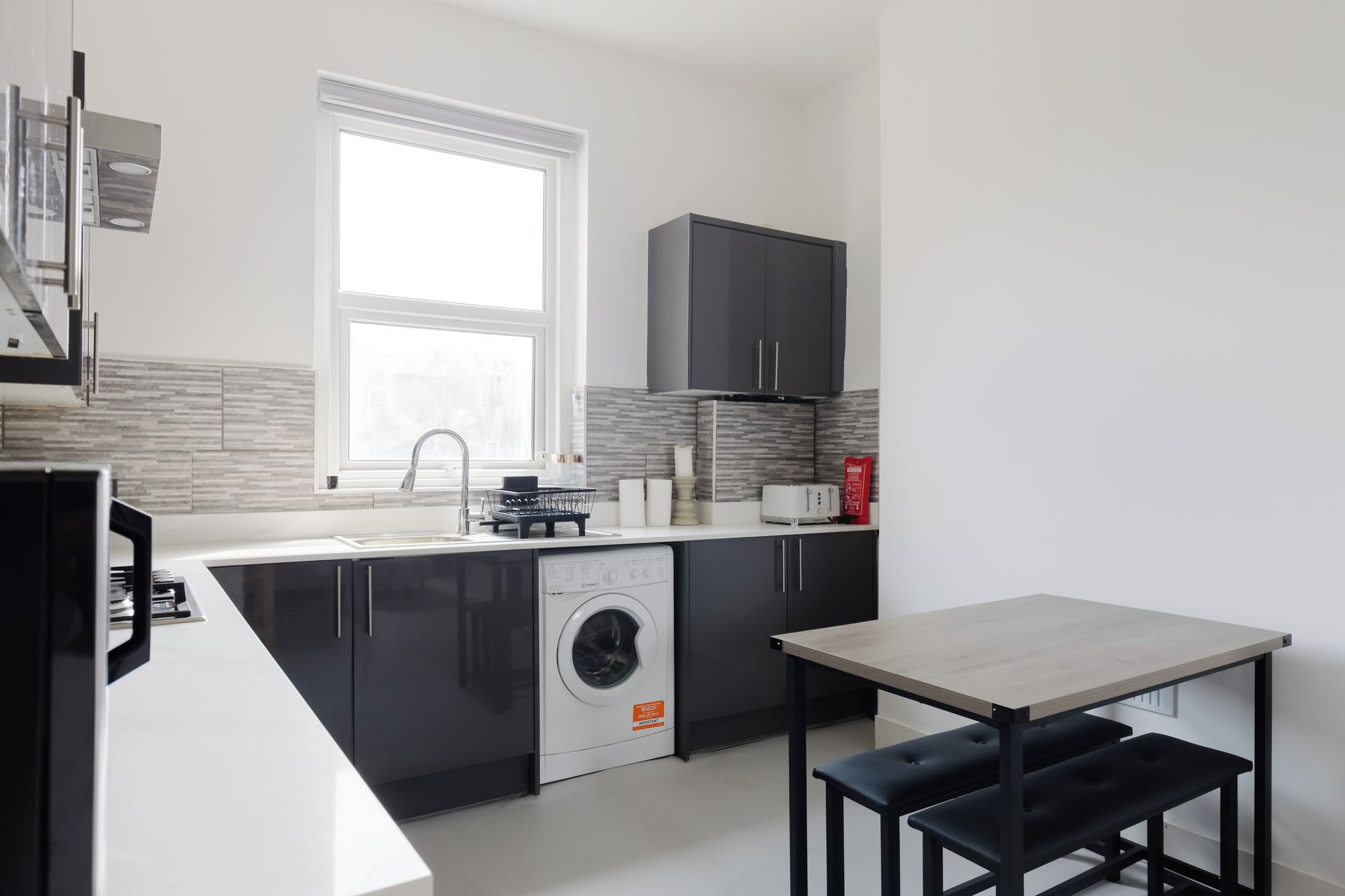 A modern kitchen with a built-in washing machine, a dining area with a table and benches, and a window providing natural light.