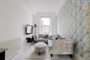 A modern living room with a sofa, ottoman, and a flat-screen TV. - Newly Renovated 4BDR Home Near Notting Hill (Greater London)