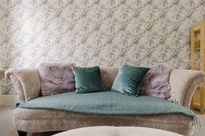 Ein Sofa vor einer Wand mit gemustertem Wandpapier und einer Holzkommode.