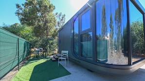 A modern house with large glass windows, a fenced yard, and a small outdoor seating area. - Guest Room “Futura 1 - House of the Future” in Borgo, 50 m from the Beach (Borgo)