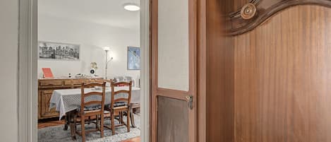 A wooden door with a textured glass panel, a dining area with a table and chairs, and a cityscape picture on the wall.