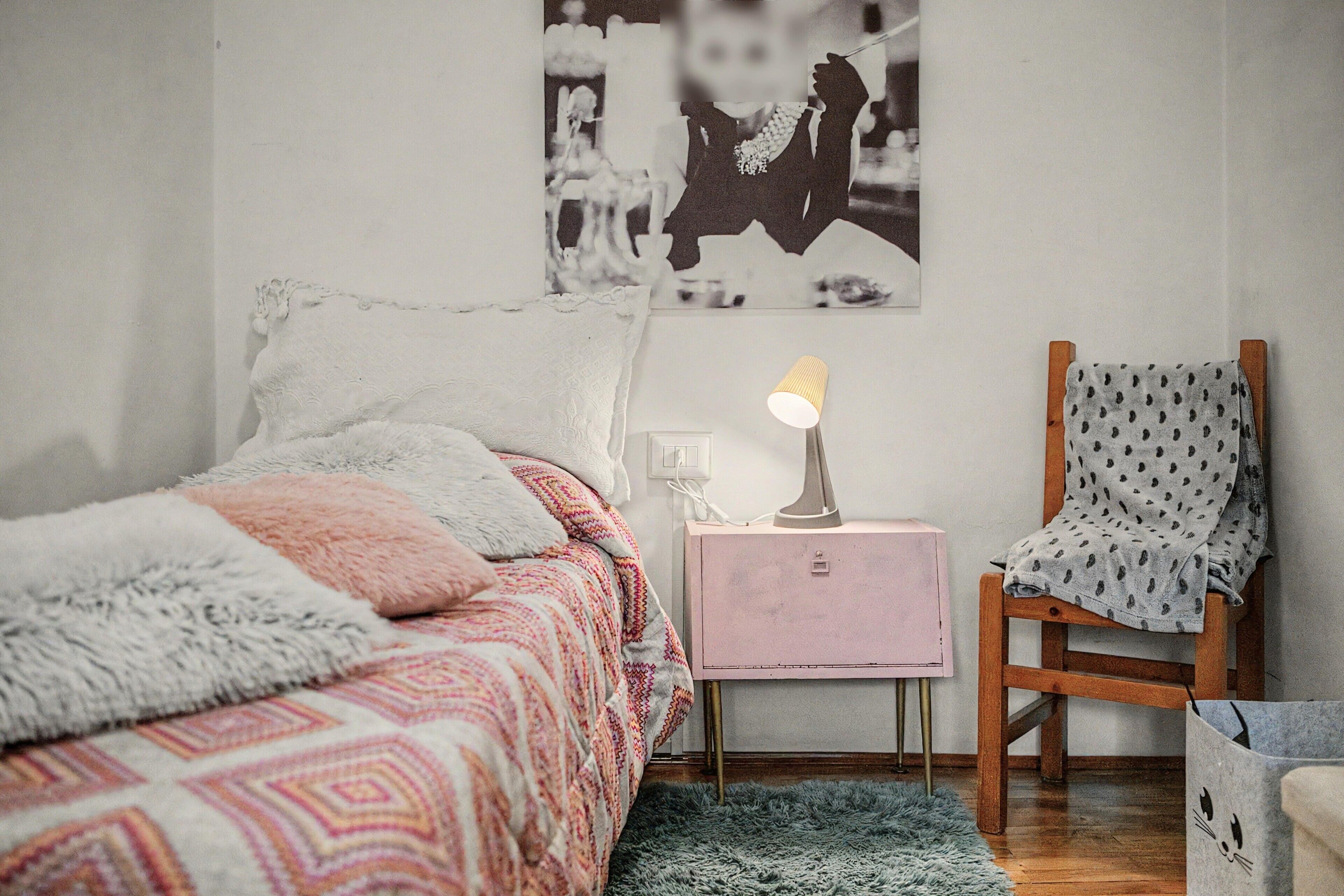 A bedroom with a bed, a chair, a nightstand, and a lamp.