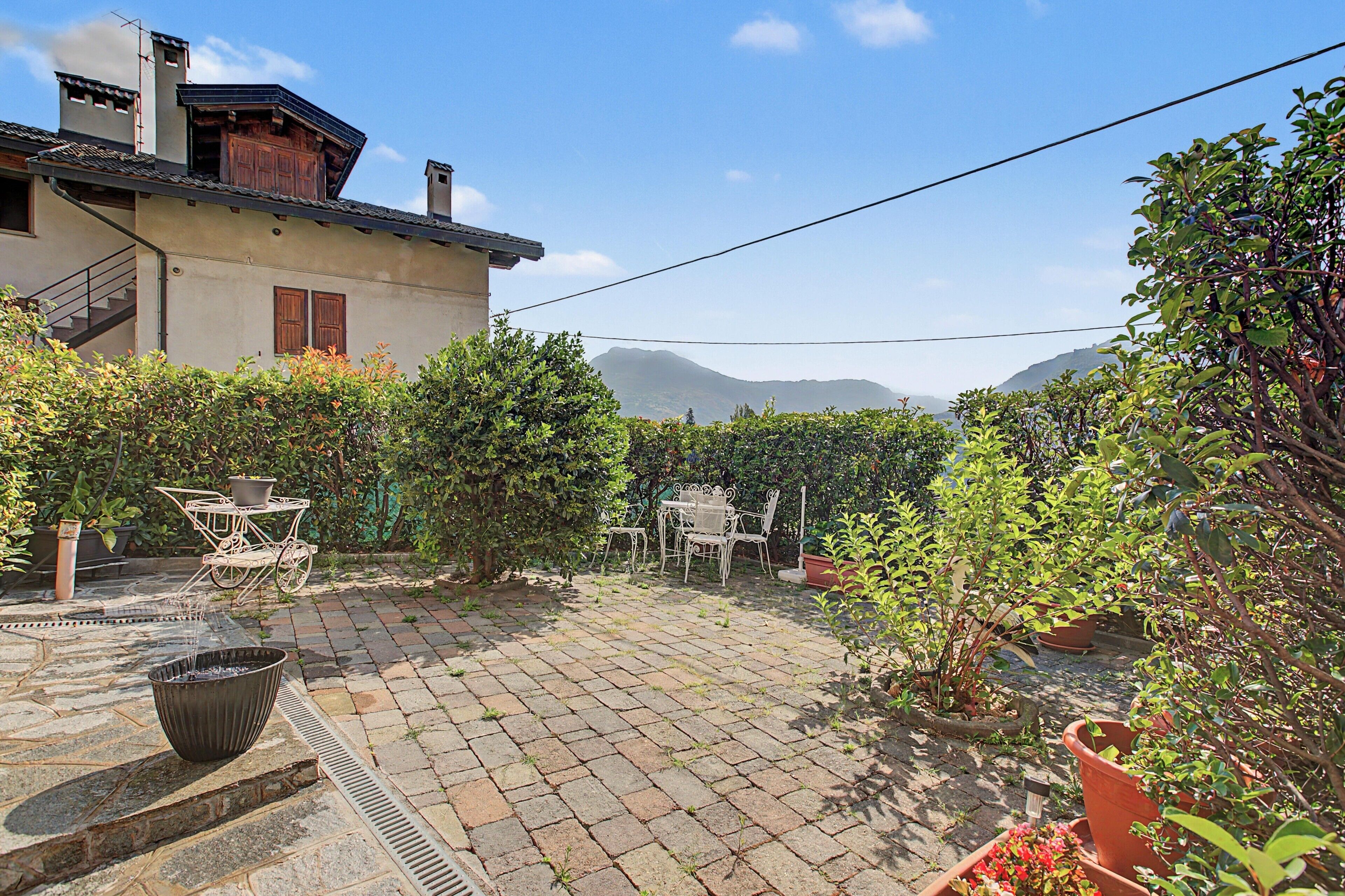 A courtyard with a paved patio, outdoor furniture, potted plants, and a view of mountains.