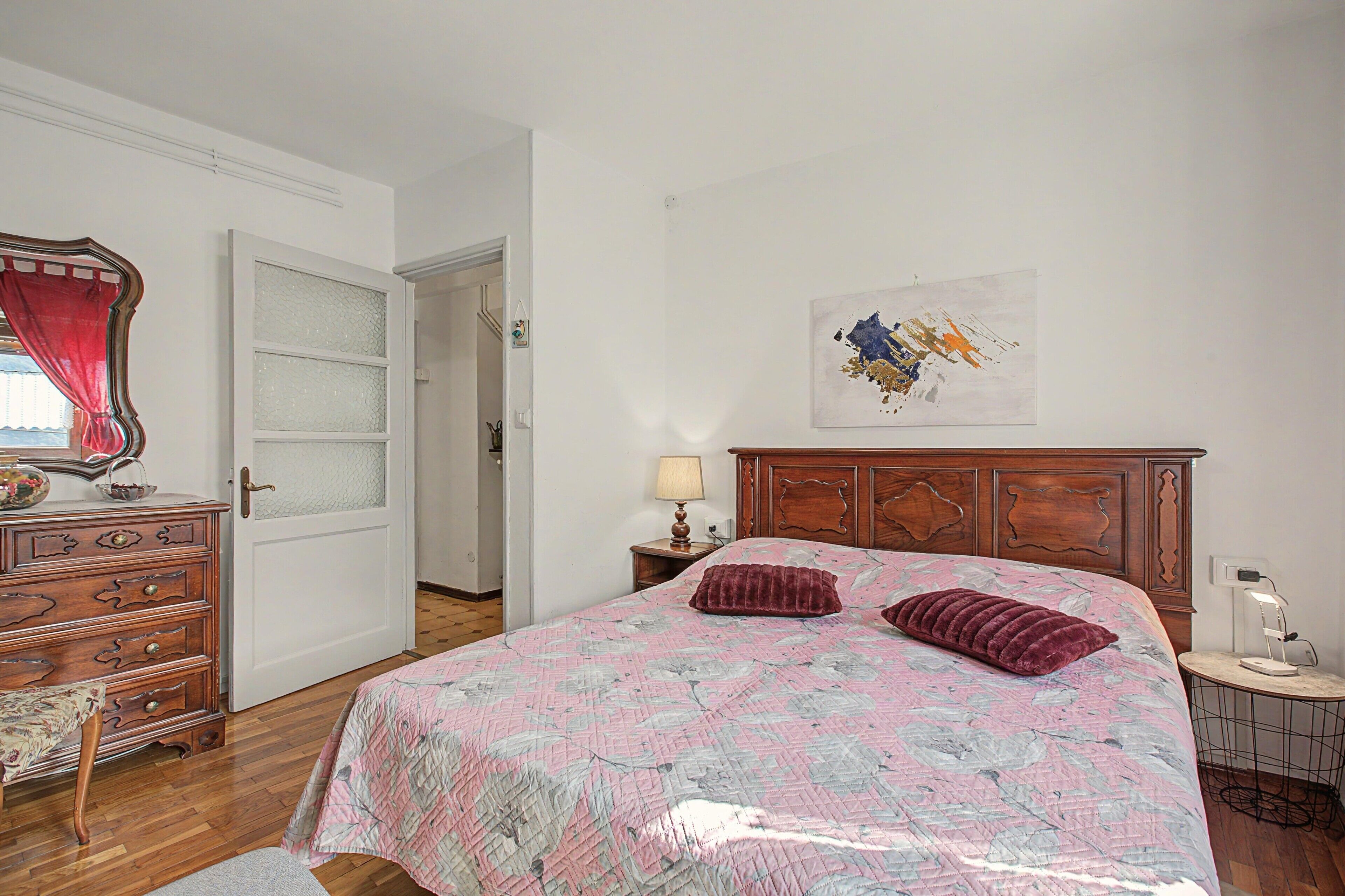 Une chambre à coucher avec un lit en bois, une commode, un miroir et un tableau accroché au mur.