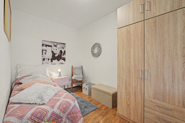 A bedroom with a bed, a chair, a small table, a wardrobe, and a wall with a picture.