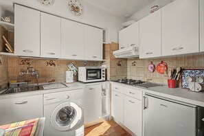 A compact kitchen with white cabinets, a washing machine, a microwave, and a gas stove. - Casa Zio Zeffy Apartment with Mountain View Balcony and Shared Garden (Châtillon)