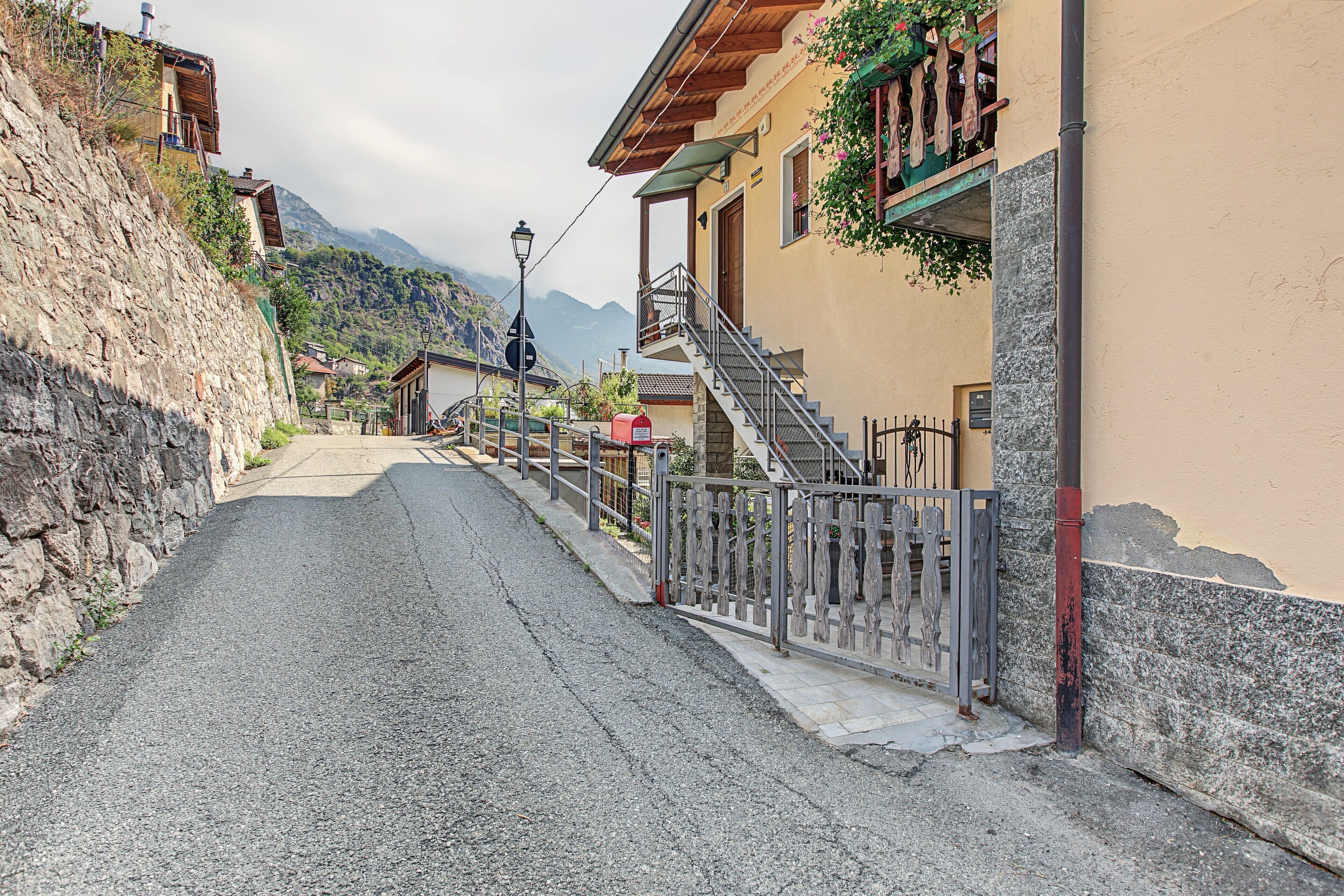 Una calle estrecha con un muro de piedra a un lado y un edificio con una escalera de madera al otro.