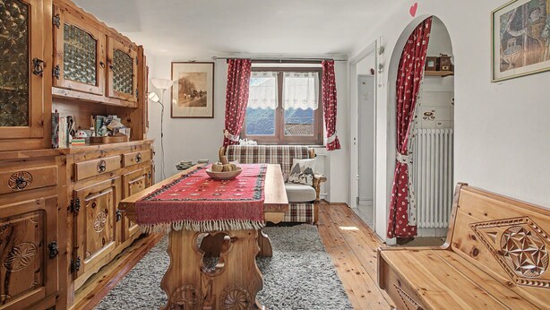 Una habitación tradicional con muebles de madera, una mesa de comedor y una ventana con cortinas.