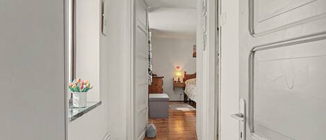 A hallway leading to a bedroom with a bed, bedside table, lamp, and a small nightstand.