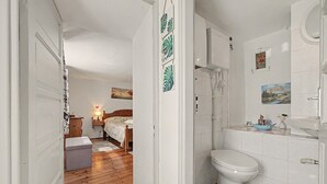 Un dormitorio con piso de madera, una cama con colcha floral, una mesita de noche con lámpara y una pared con un cuadro enmarcado.