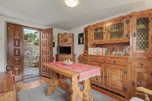 A wooden dining table with a red tablecloth, surrounded by wooden cabinets with glass doors, a television, and a stone wall outside.