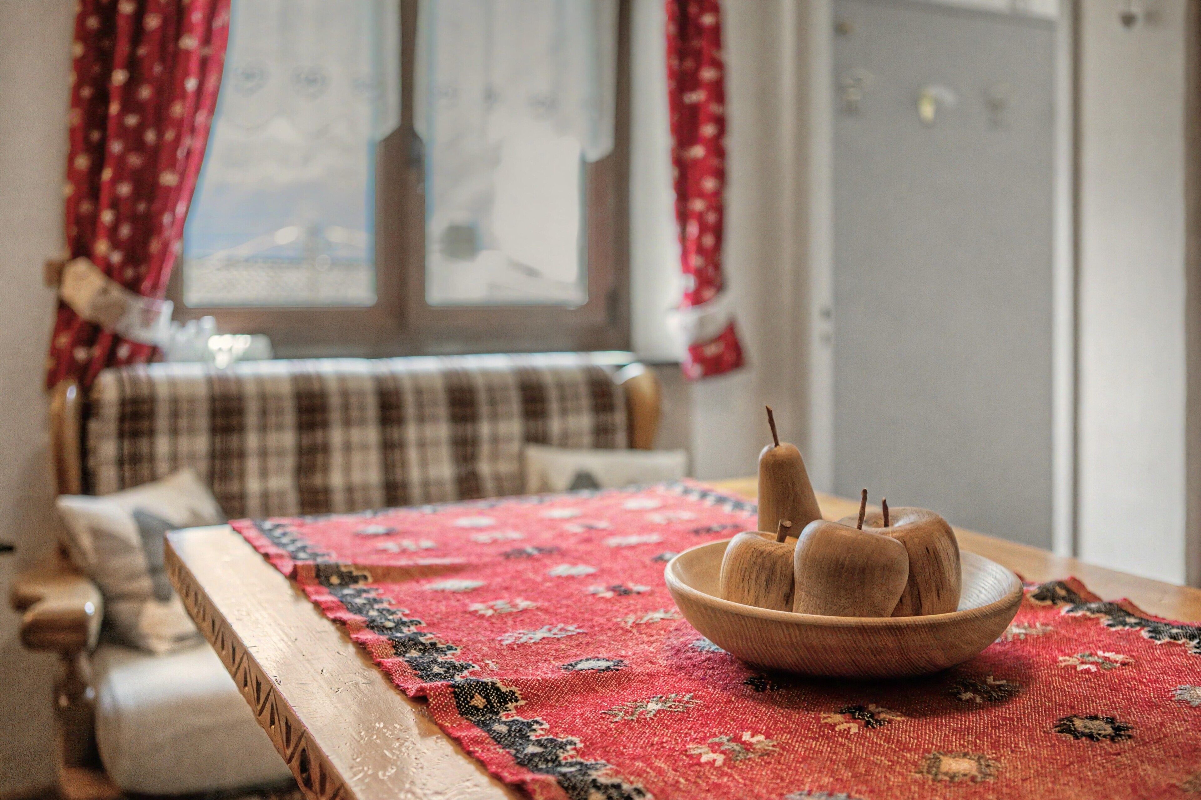 Een kamer met een houten tafel, een tapijt met rood patroon en een raam met gordijnen.