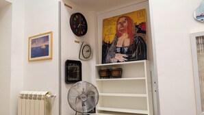 Une pièce avec un radiateur, une horloge murale, un ventilateur, une étagère avec des boîtes de rangement et un tableau encadré.