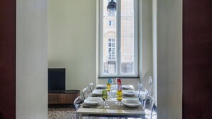 A dining area with a table set for six, a television in the background, and a window with a view of buildings. - The Gallery House by Wonderful Italy (Genova)