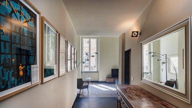 A hallway with framed artwork, a large mirror, and a seating area with a chair and a small table. - The Gallery House by Wonderful Italy (Genova)