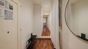 Un pasillo con suelo de madera, paredes blancas, un escritorio negro, un espejo y una puerta con un mapa.