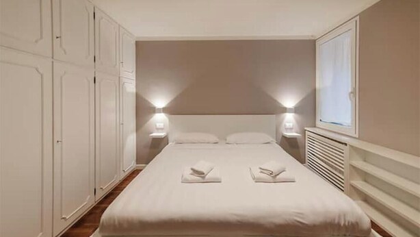 Un dormitorio con cama, mesitas de noche, una ventana y un armario.