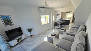 En moderne stue med et fladskærms-tv, et spiseområde og et køkken i baggrunden.