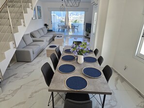 A modern living area with a sofa, dining table, chairs, and a staircase. - Villa Catherine, Paphos 150 metres from Venus Beach – come and visit us. (PAFOS)