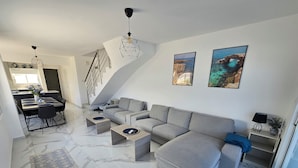 En moderne stue med en grå hjørnesofa, et spisebord med stole, en trappe og to billeder i rammer på væggen.