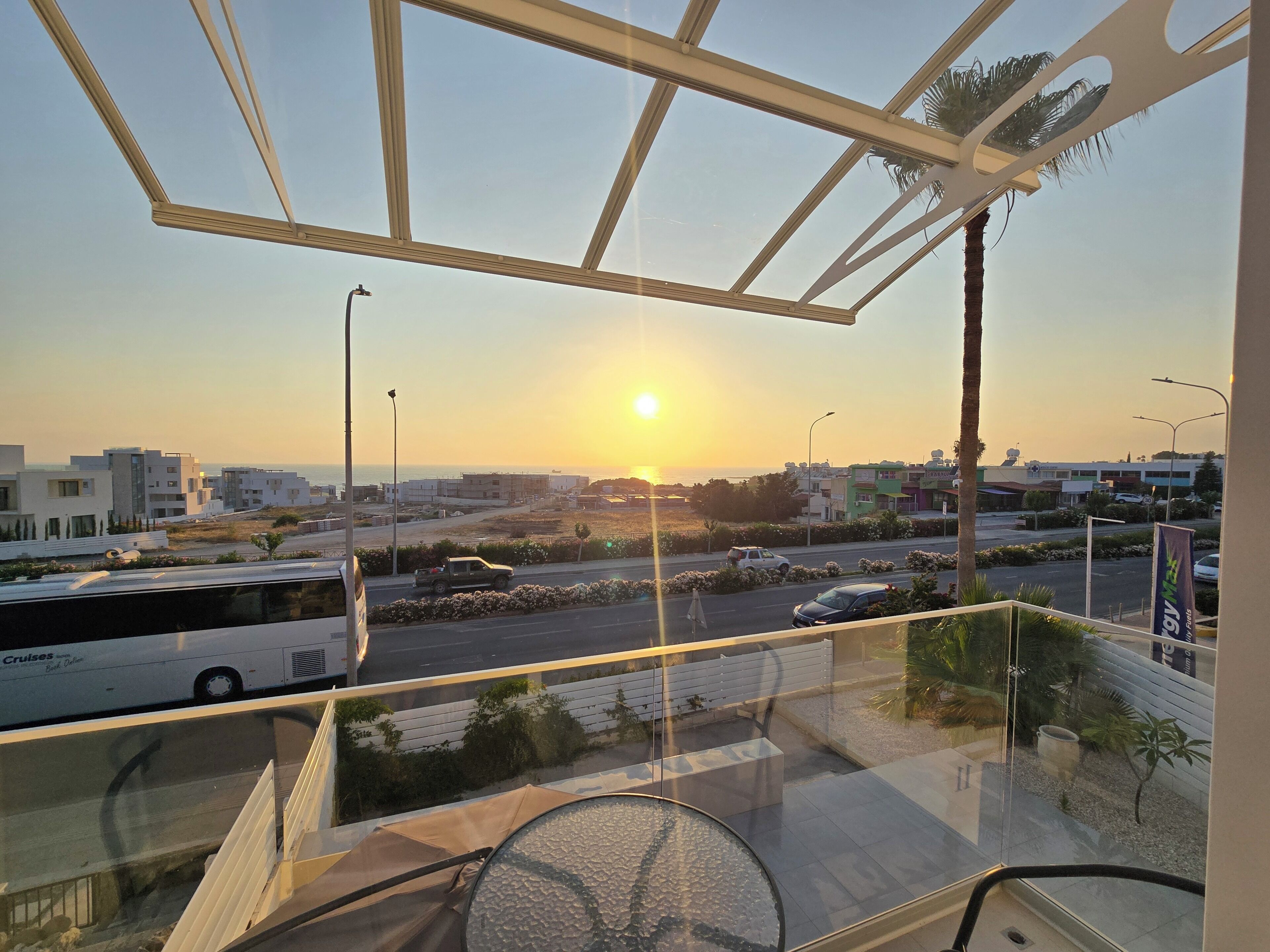 A balcony with a view of the sunset, a road with vehicles, and modern buildings in the distance.