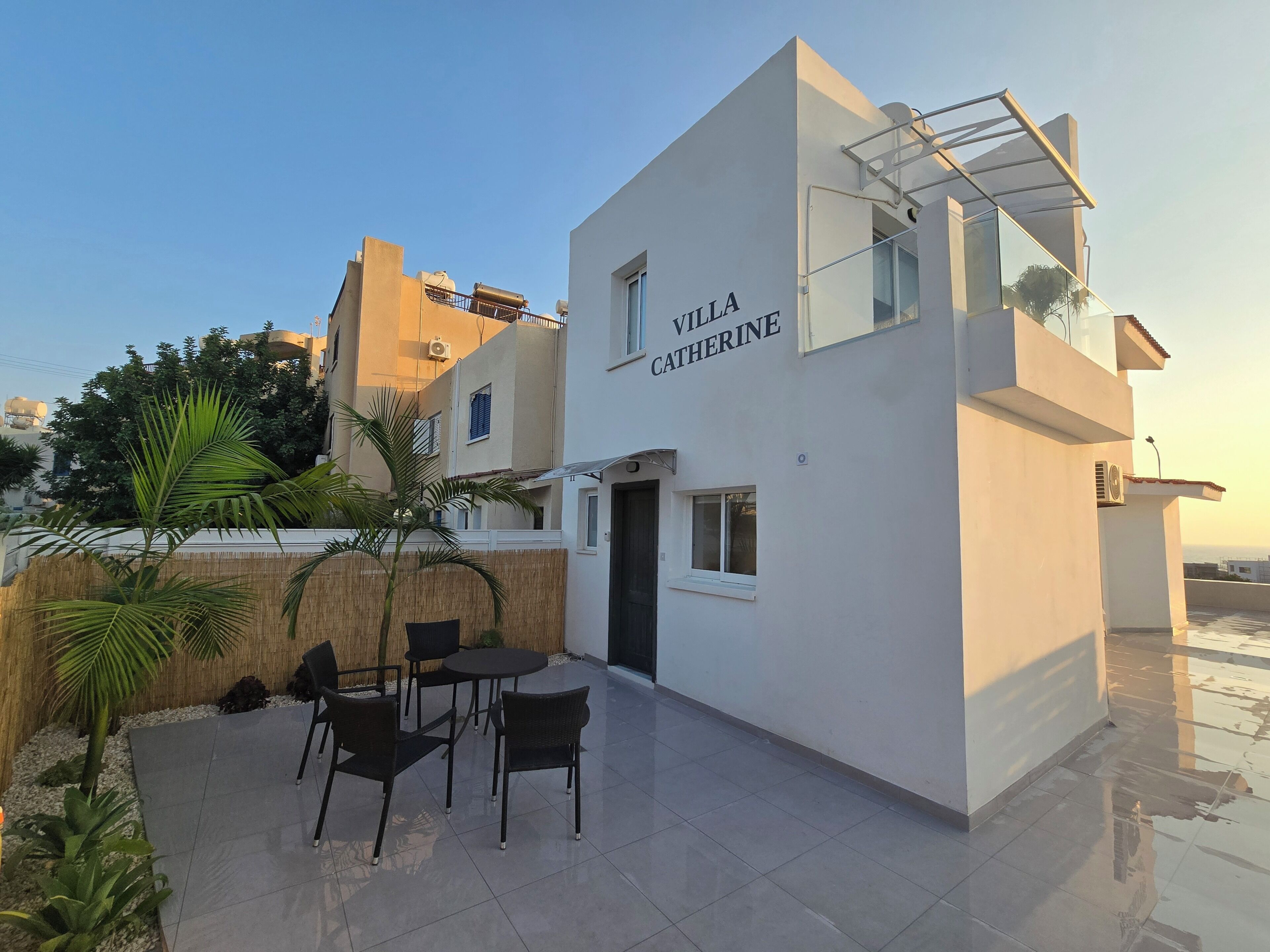 A modern building with the name 'Villa Catherine' on the facade, a patio with chairs, and a clear sky.