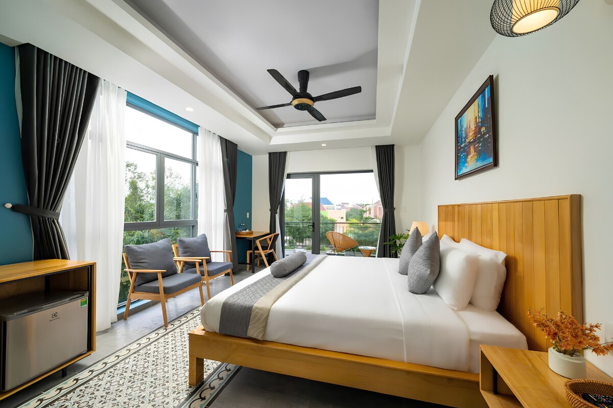 A modern hotel room with a large bed, a desk, a chair, and a balcony with a view.
