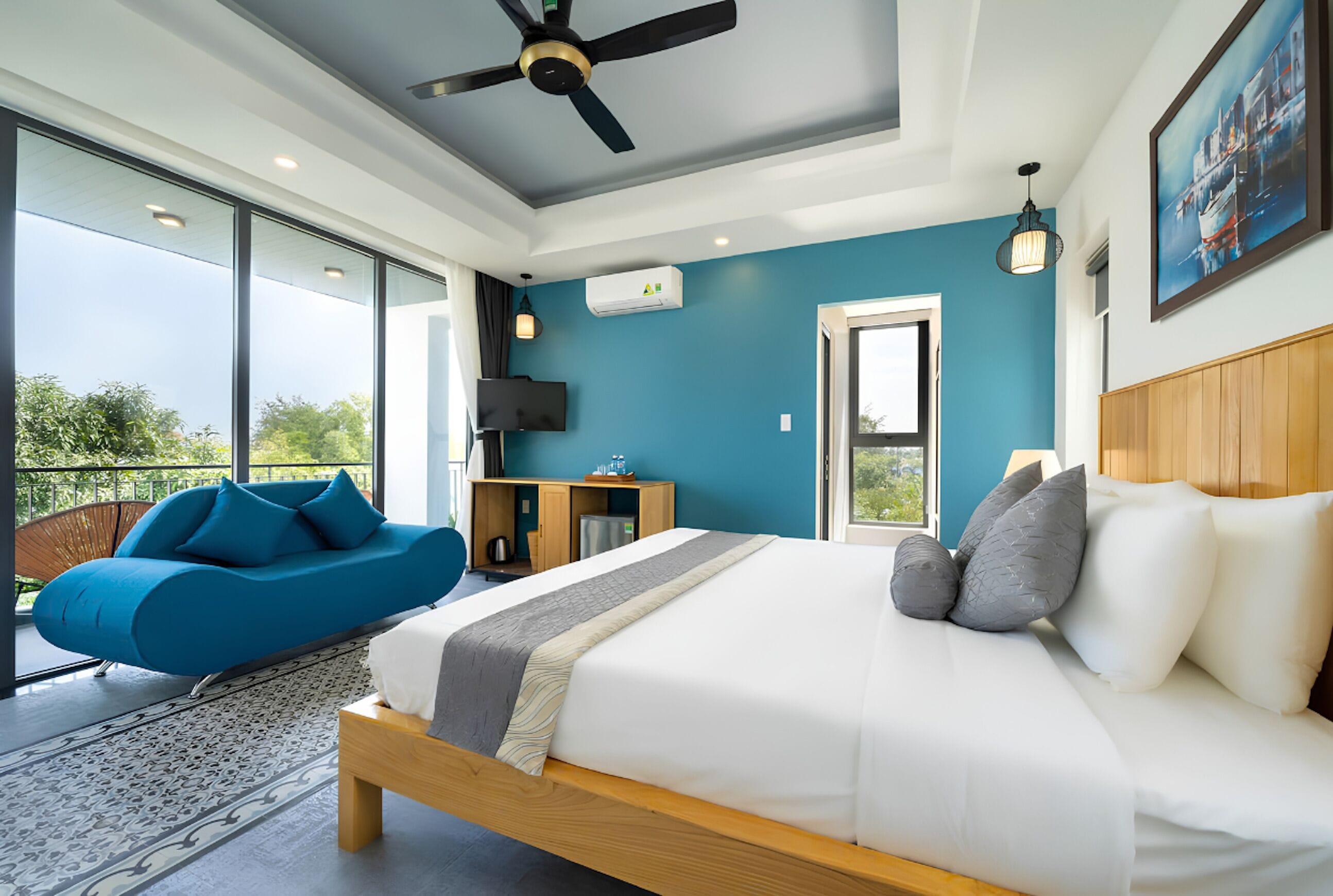 A modern bedroom with a bed, a blue sofa, a television, and a view of the outdoors.