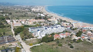 Vista aèria d'una vila costanera amb un hotel a primera línia de platja, un edifici gran amb teulada plana i zones residencials als voltants.