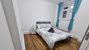 Un dormitori amb un llit, una tauleta de nit, una finestra amb cortines i un radiador.