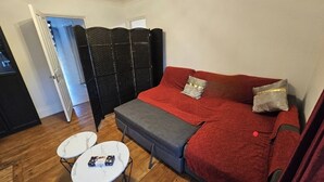 Una habitació amb un sofà vermell, una banca grisa, dues taules petites blanques i una partició negra.