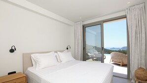 A bedroom with a large bed, a nightstand, a chair, and a view of a balcony with outdoor furniture. - Villa Noema, Luxury Villa (Corfu)