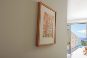Ein gerahmtes Kunstwerk an einer Wand, eine Steinwand und ein Poolbereich mit Meerblick.
