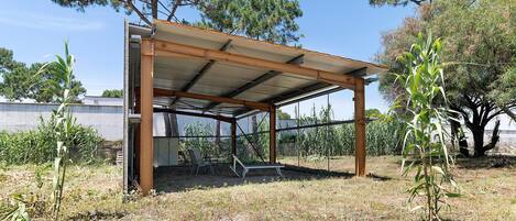 A covered outdoor area with a metal roof, surrounded by trees and vegetation.