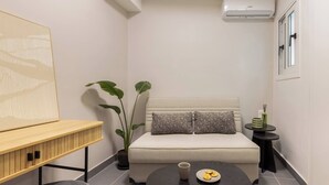 Ein modernes Zimmer mit einer Couch, einem kleinen runden Tisch mit einem Teller Keksen, einer Topfpflanze und einer Wand-Klimaanlage.