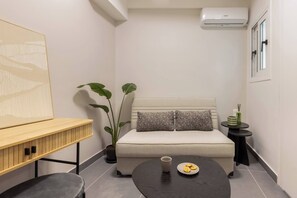 A modern room with a sofa, a small round table with a plate of cookies, a potted plant, and a wall-mounted air conditioner. - Charokopou3 - Elegant Urban Flat Near Center (Kallithea)