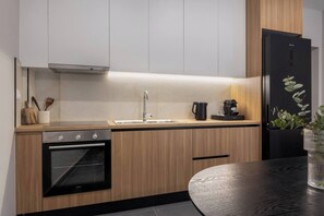 A modern kitchen with wooden cabinets, a black oven, a sink, and a refrigerator. - Charokopou3 - Elegant Urban Flat Near Center (Kallithea)
