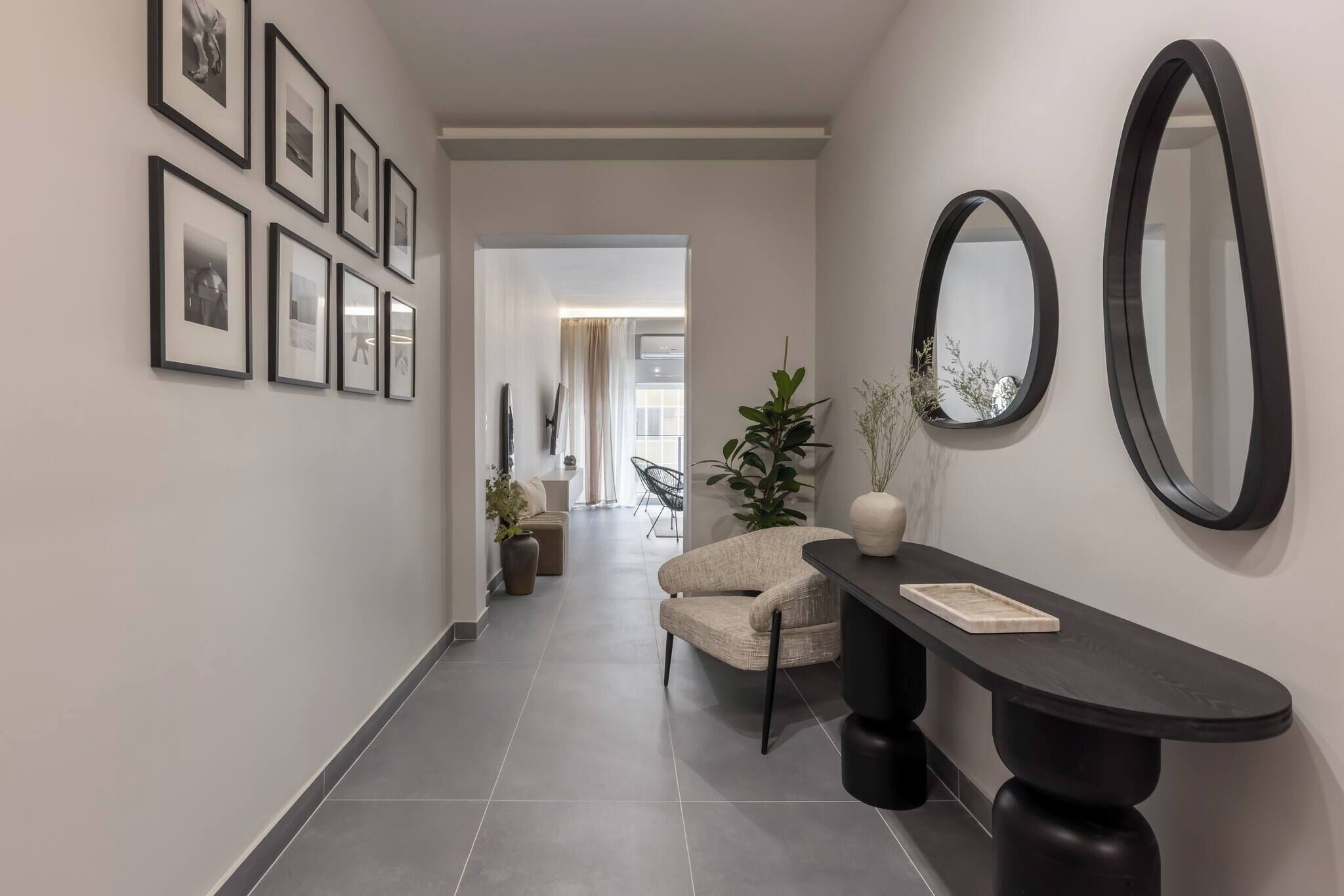 A hallway with framed pictures on the wall, a chair, a console table, and a mirror.