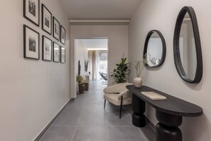 A hallway with framed pictures on the wall, a chair, a console table, and a mirror. - Charokopou3 - Elegant Urban Flat Near Center (Kallithea)