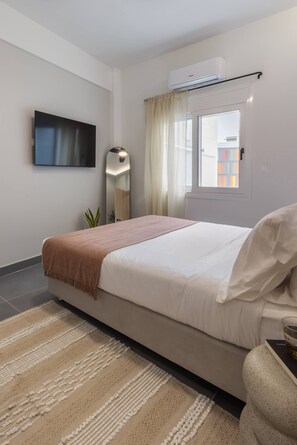 A modern bedroom with a bed, a TV, a window with curtains, and an air conditioning unit. - Charokopou3 - Elegant Urban Flat Near Center (Kallithea)