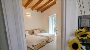 A bedroom with two beds, wooden flooring, a ceiling with exposed beams, and a window. - Villa surrounded by nature · Complete privacy · Views of the sea and mountains (Orosei)