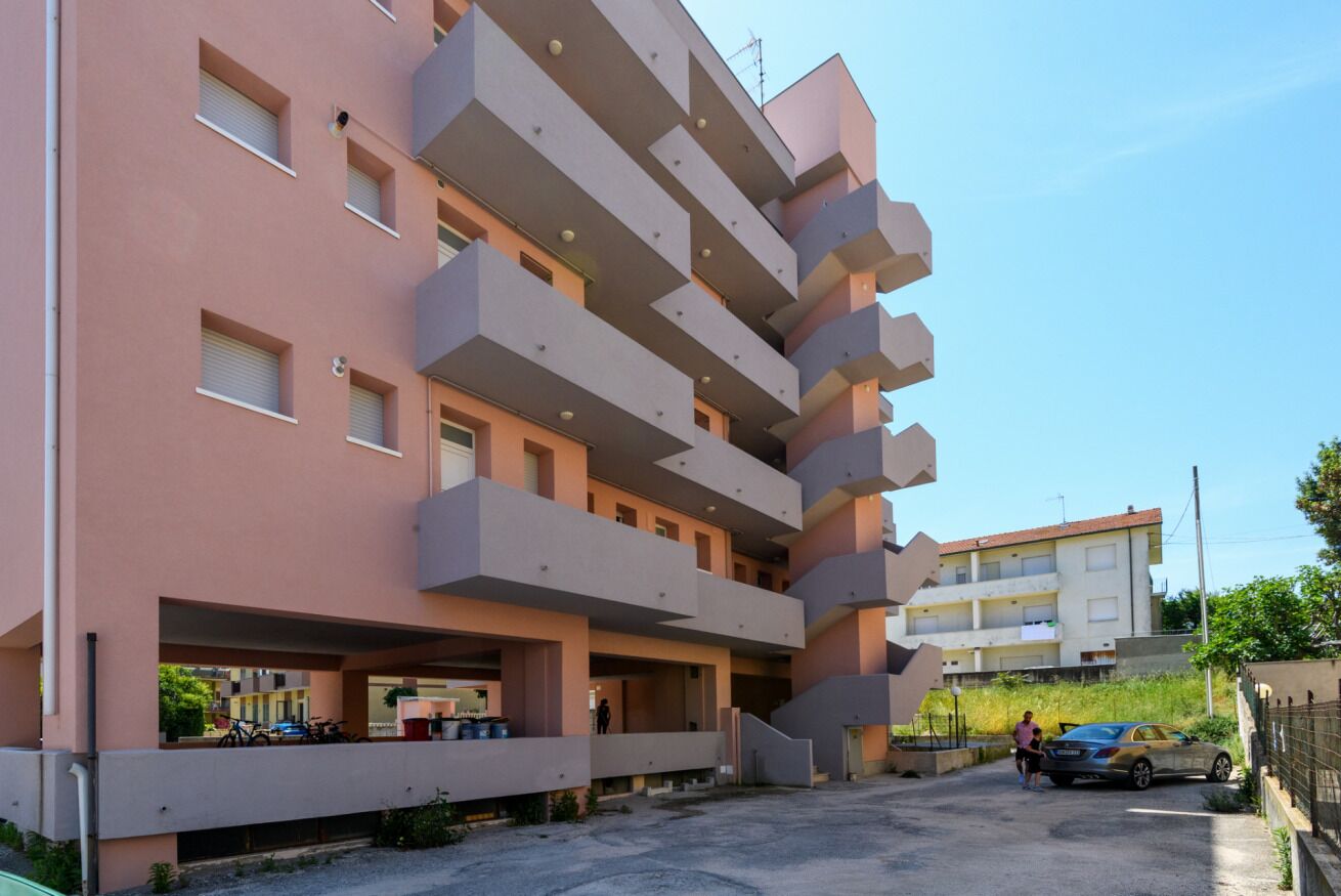 Un edificio a più piani con balconi, un'area di parcheggio e un edificio adiacente.