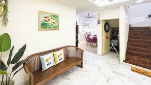 A room with a wooden bench, a ceiling fan, a dining area, and a kitchen visible through an open door. - My Garden House USJ by Airhost (Subang Jaya)