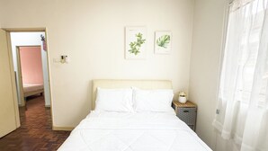 A hotel room with a bed, a nightstand with a vase of flowers, and two framed botanical illustrations on the wall. - My Garden House USJ by Airhost (Subang Jaya)
