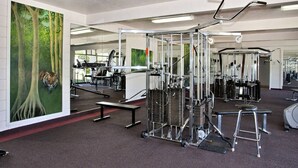 Un gimnasio con diferentes máquinas de ejercicio, un espejo grande y un cuadro de un tigre en la pared.