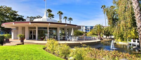 A modern building with a covered patio, a flagpole, and a pond with a fountain.