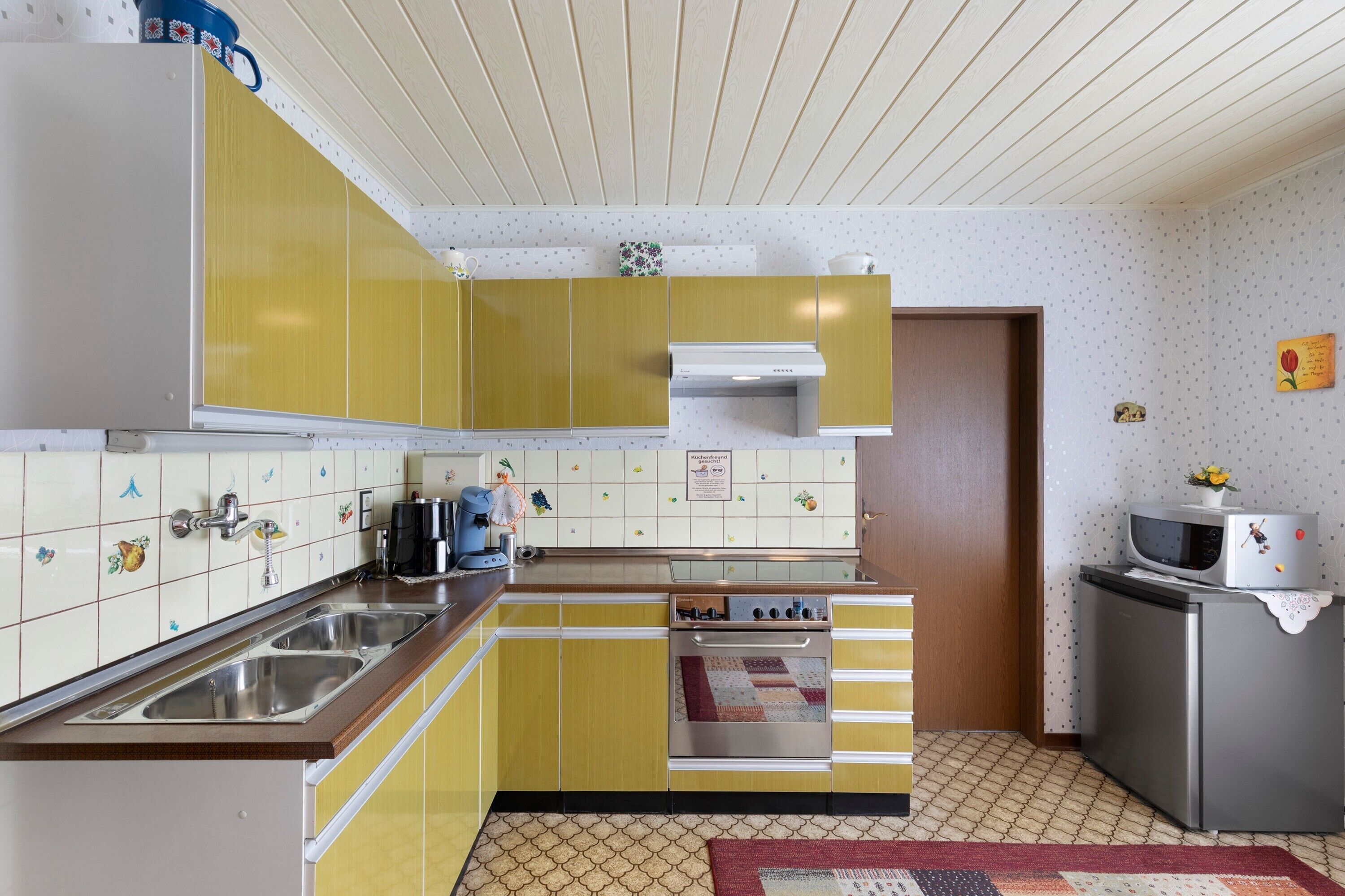 Una cocina con gabinetes amarillos, un lavamanos de acero inoxidable, un microondas y un refrigerador.