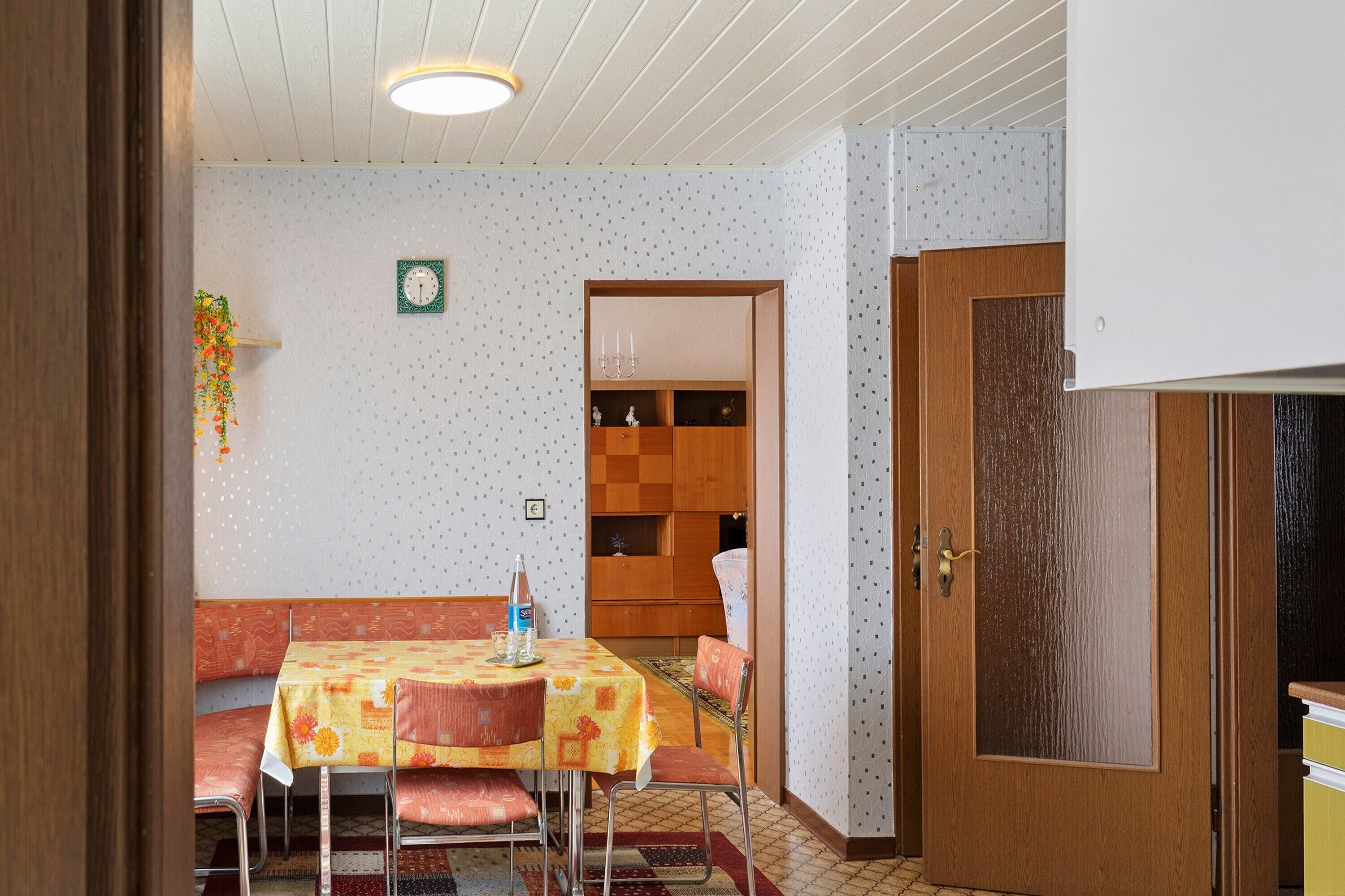 A dining area with a table and chairs, a wooden cabinet, and a patterned wall.
