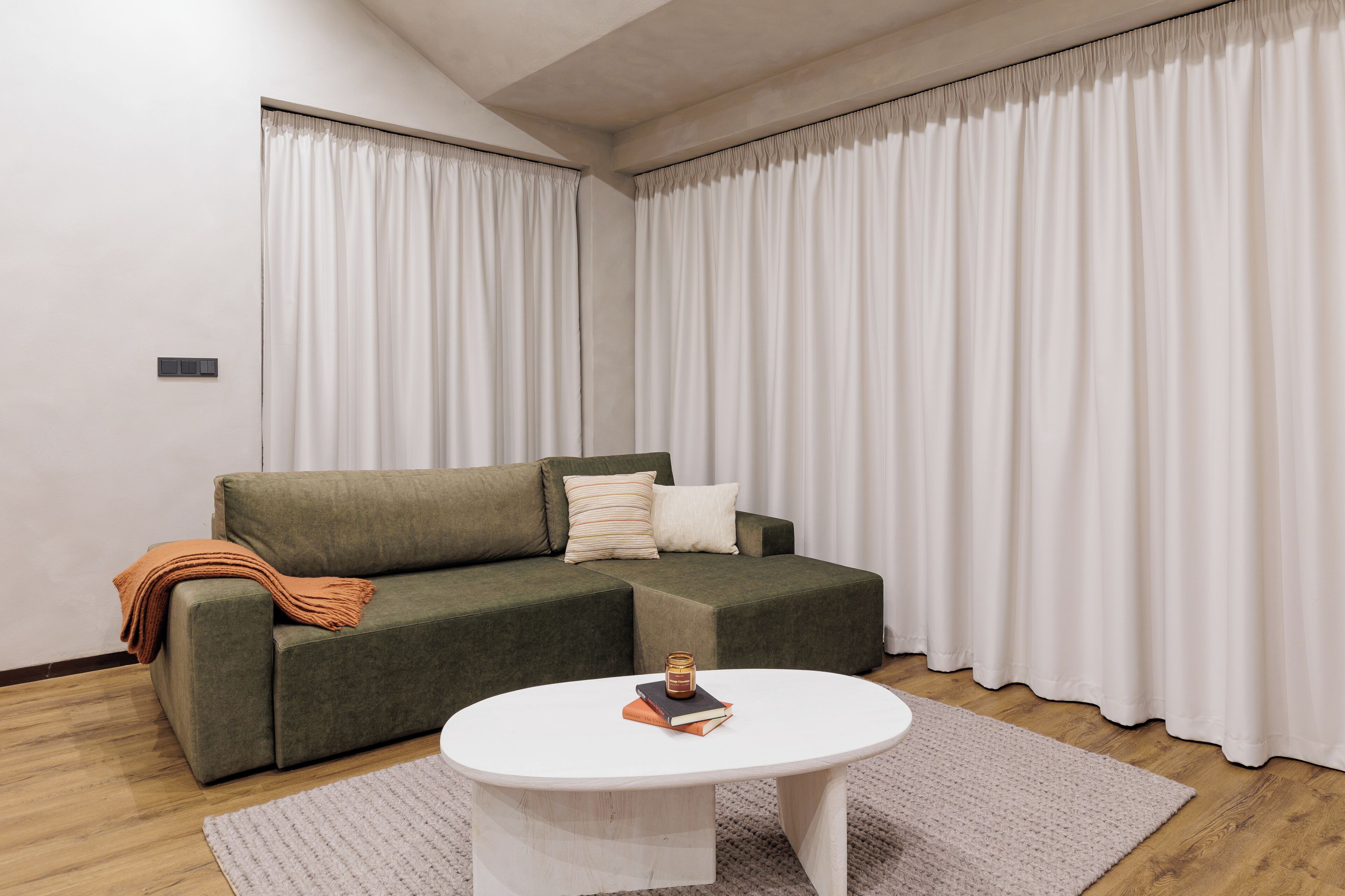 Un salon moderne avec un canapé d’angle, une table basse ronde et une grande fenêtre agrémentée de rideaux blancs.